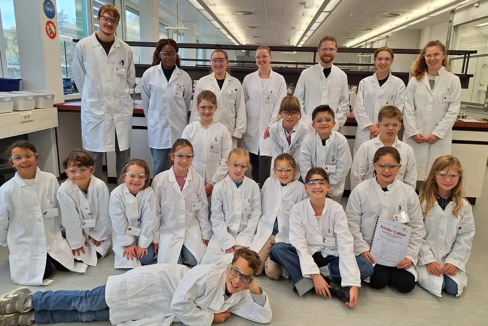 Gruppenbild im Chemie-Labor der Lebensmitteltechnik Hochschule Trier mir Teilnehmern und Helfern des Kinderlabors 2025, es tragen alle Kittel und Schutzbrille